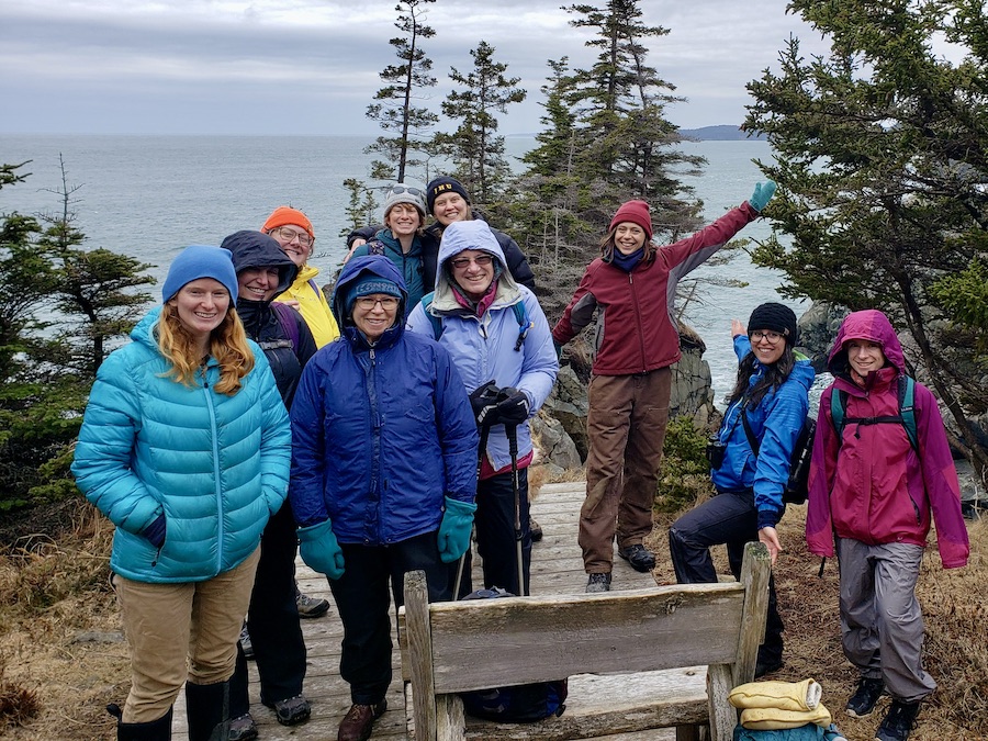 group of women smiling on top of a cliff